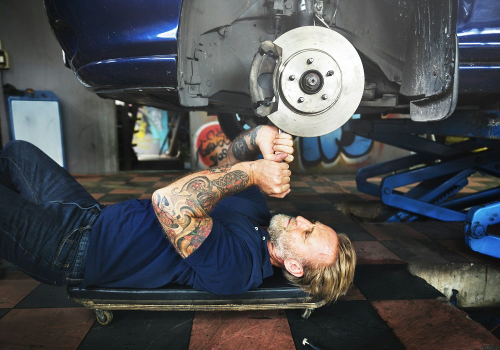 Caucasian auto mechanic man lying reparing car disc brake in garage